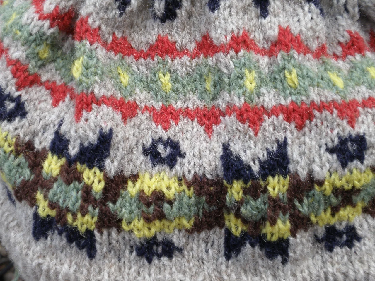 Close-up of a multi-colour patterned knit — red, green, yellow and navy motifs formed stitch by stitch in bands across a cream ground.