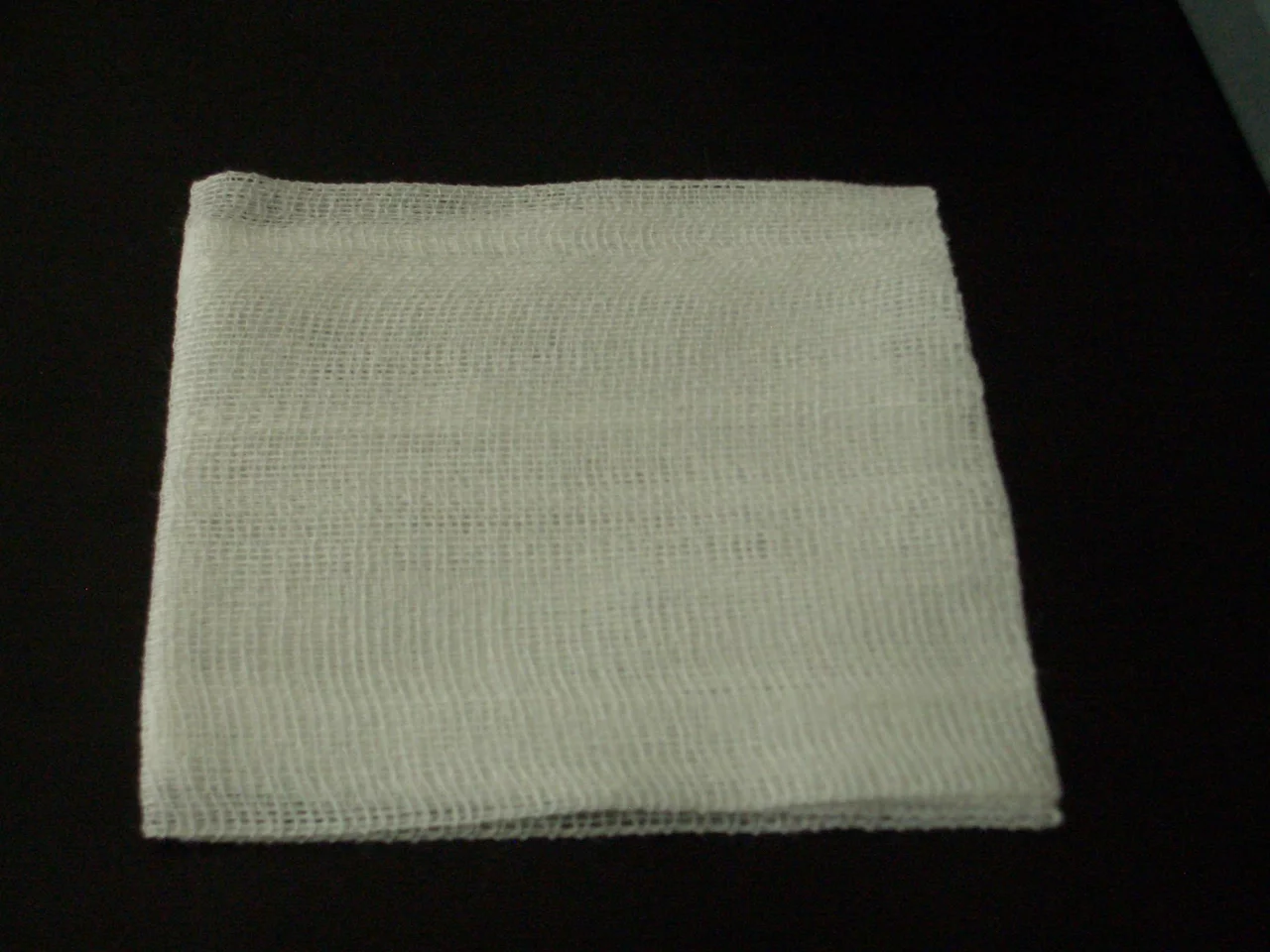 Close-up of a soft white cotton gauze, the open crimped weave and its layers filling the frame.