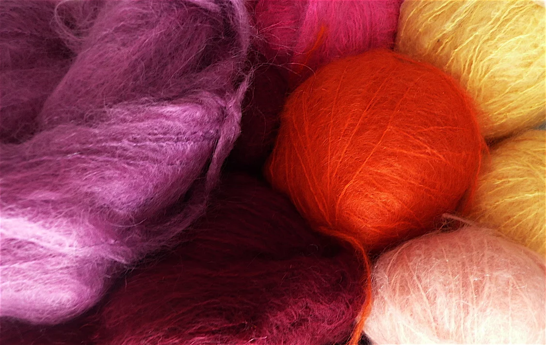 Close-up of balls of brushed mohair yarn in pink, red, orange and yellow, a fibre halo standing off each one.