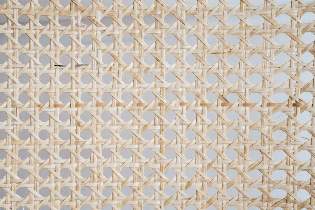Close-up of a natural rattan cane sheet, flat splints crossing in an open hexagonal weave.