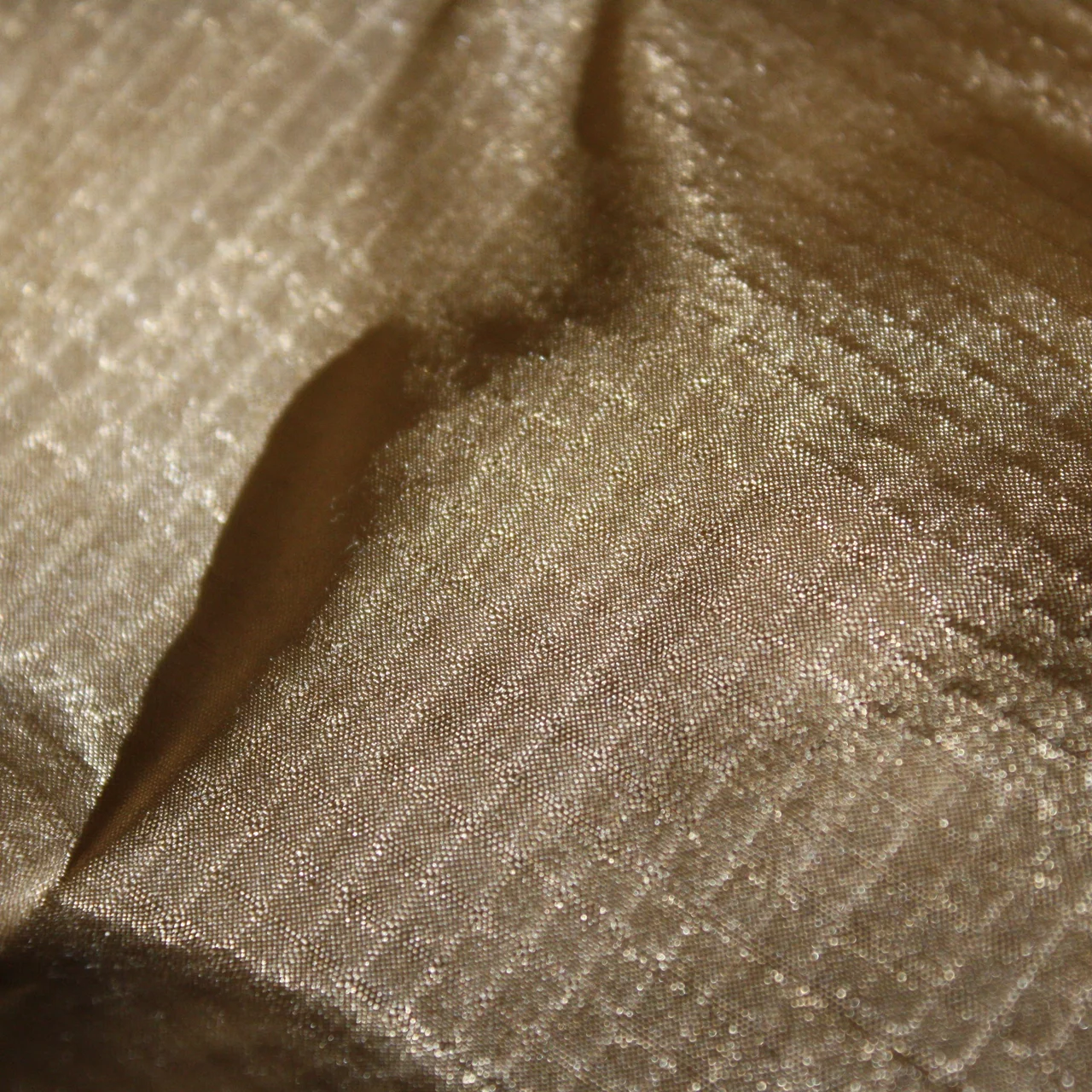 Macro close-up of tan ripstop nylon, the heavier reinforcement yarns forming a square grid across the fine ground.